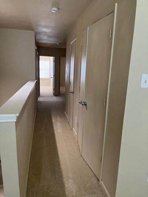 corridor with light carpet and a textured ceiling