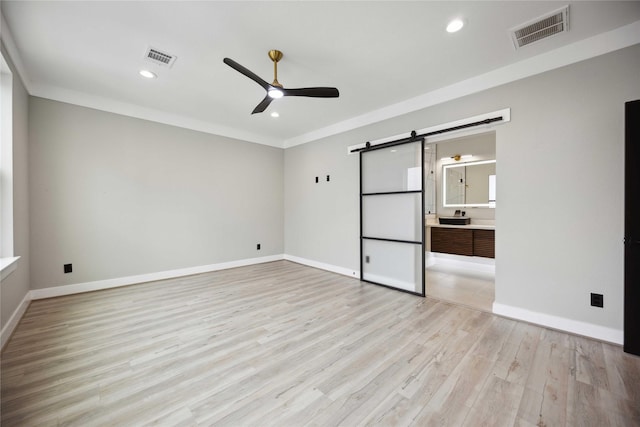 unfurnished bedroom featuring connected bathroom, ceiling fan, a barn door, light hardwood / wood-style flooring, and crown molding