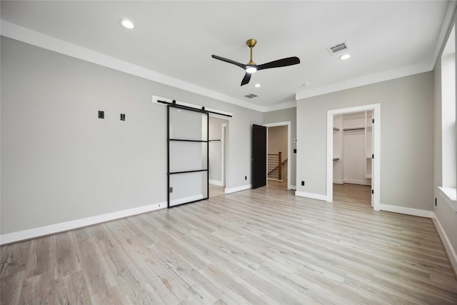 unfurnished bedroom featuring crown molding, ceiling fan, a barn door, a spacious closet, and a closet