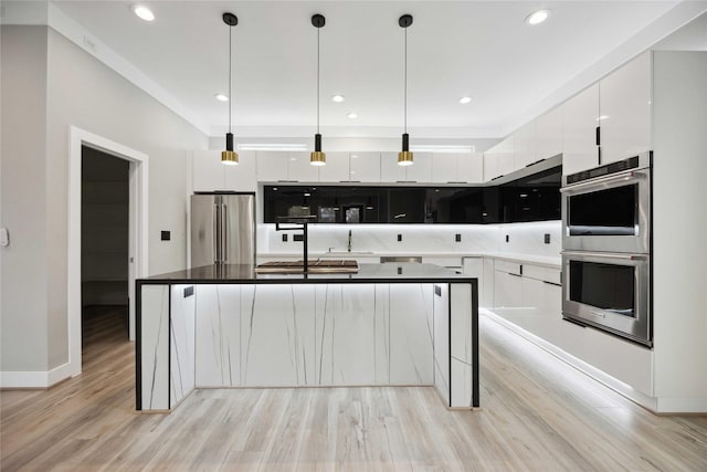 kitchen with white cabinets, a center island with sink, light wood-type flooring, appliances with stainless steel finishes, and decorative light fixtures