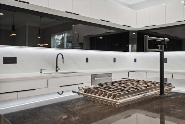 interior space with stainless steel dishwasher, cooktop, white cabinetry, and sink