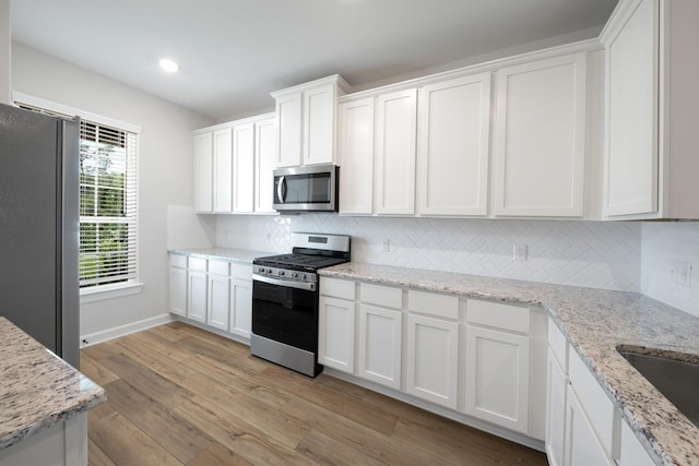 kitchen with white cabinets, light hardwood / wood-style flooring, decorative backsplash, appliances with stainless steel finishes, and light stone counters