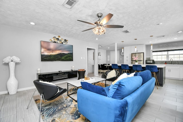 tiled living room with a textured ceiling, ceiling fan, and sink