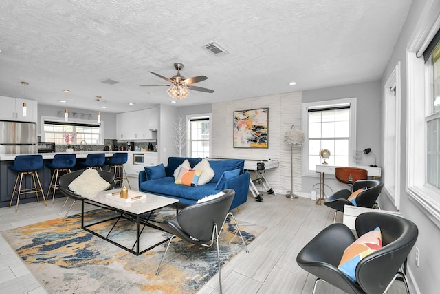 living room with ceiling fan, sink, a healthy amount of sunlight, and a textured ceiling