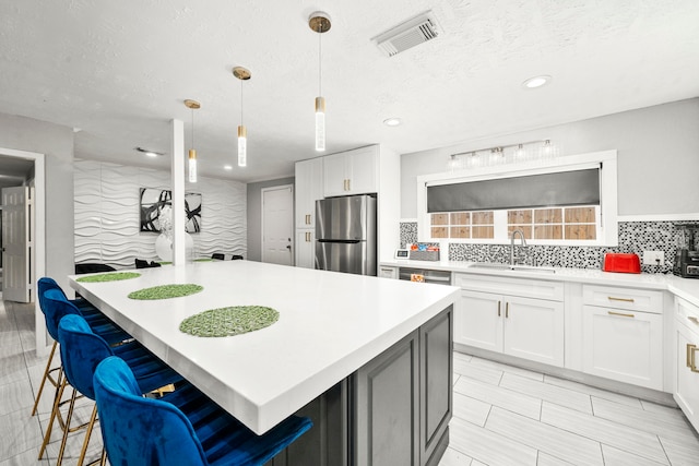 kitchen with white cabinetry, stainless steel fridge, sink, and decorative light fixtures