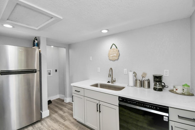 kitchen featuring stainless steel refrigerator, dishwasher, sink, a textured ceiling, and light wood-type flooring