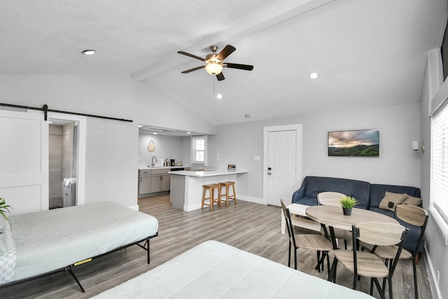 bedroom featuring ceiling fan, a barn door, vaulted ceiling with beams, light hardwood / wood-style flooring, and ensuite bathroom