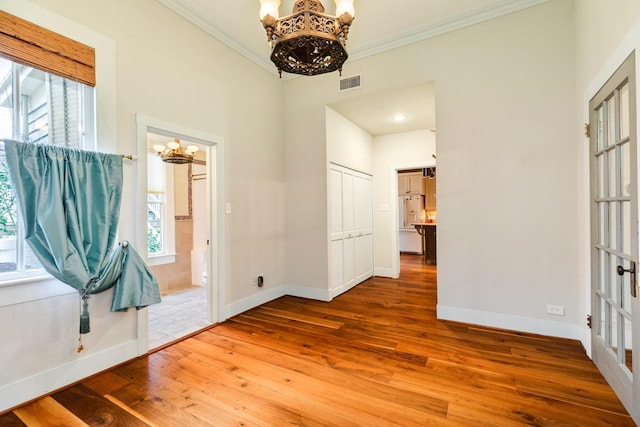 interior space with a notable chandelier, hardwood / wood-style flooring, ornamental molding, and a healthy amount of sunlight