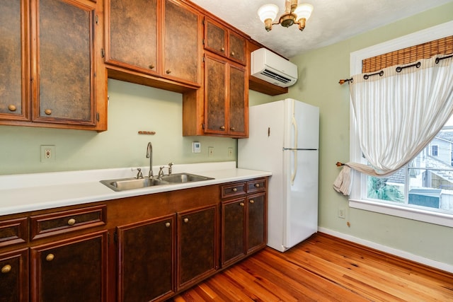 kitchen featuring sink, an inviting chandelier, a wall unit AC, white refrigerator, and wood-type flooring