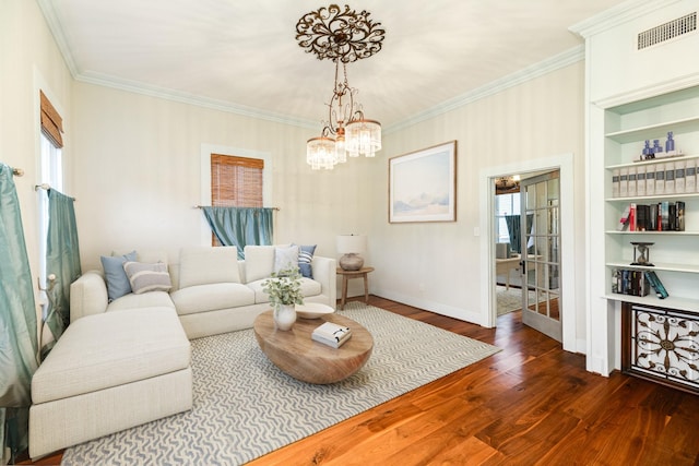 living room featuring dark hardwood / wood-style flooring, built in shelves, ornamental molding, and an inviting chandelier