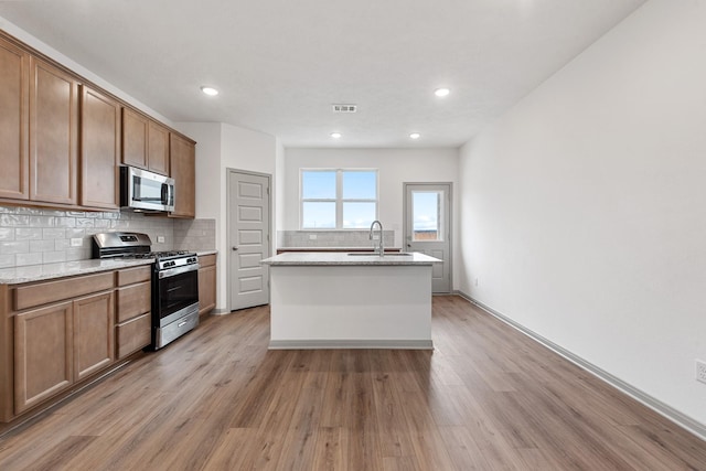 kitchen featuring light hardwood / wood-style flooring, an island with sink, decorative backsplash, appliances with stainless steel finishes, and sink