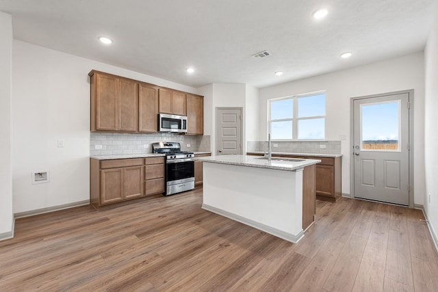 kitchen featuring sink, light stone counters, light wood-type flooring, a kitchen island with sink, and appliances with stainless steel finishes