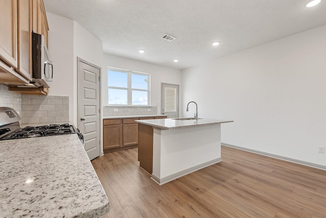 kitchen featuring a center island with sink, stainless steel appliances, light wood-type flooring, light stone counters, and sink