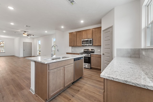 kitchen with stainless steel appliances, sink, light stone counters, ceiling fan, and backsplash