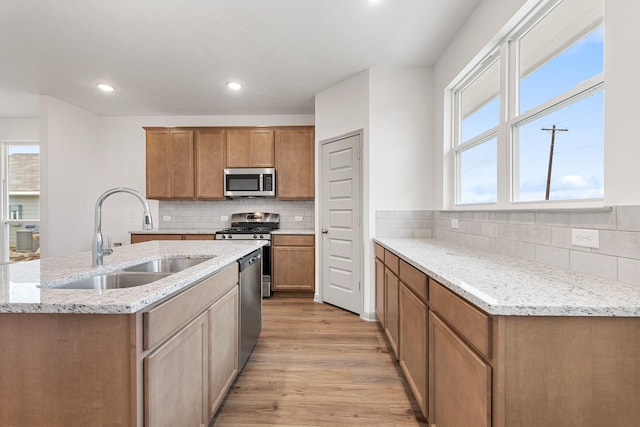 kitchen with light stone countertops, light hardwood / wood-style floors, tasteful backsplash, appliances with stainless steel finishes, and sink