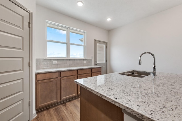 kitchen with sink, decorative backsplash, hardwood / wood-style floors, and light stone countertops