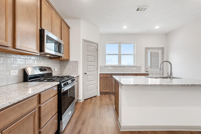 kitchen featuring stainless steel appliances, sink, light stone countertops, and an island with sink