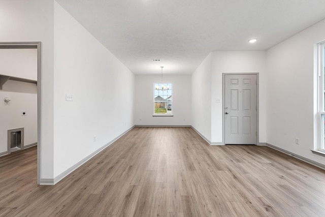 empty room with light wood-type flooring and an inviting chandelier