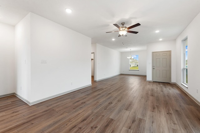 empty room featuring ceiling fan with notable chandelier and dark hardwood / wood-style floors