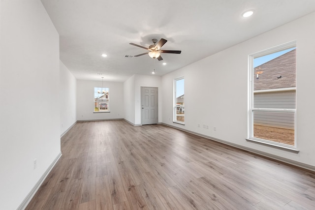 empty room featuring ceiling fan with notable chandelier and light wood-type flooring