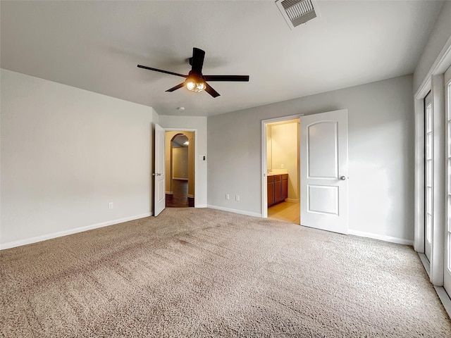 unfurnished bedroom featuring light colored carpet, ensuite bath, and ceiling fan