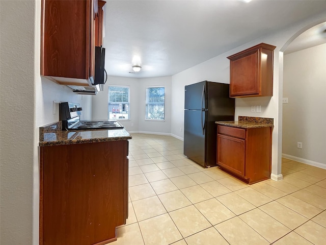 kitchen featuring black refrigerator, stove, light tile patterned floors, and dark stone countertops