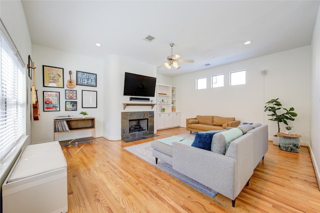 living room featuring a tile fireplace, ceiling fan, light hardwood / wood-style flooring, and a wealth of natural light