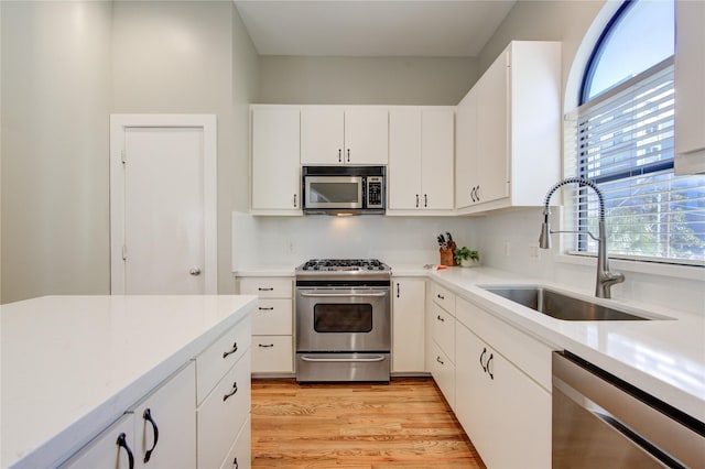 kitchen with stainless steel appliances, sink, white cabinets, light wood-type flooring, and a wealth of natural light