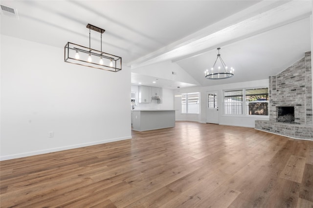 unfurnished living room featuring a fireplace, wood-type flooring, vaulted ceiling with beams, and an inviting chandelier