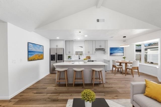 kitchen with a kitchen breakfast bar, light wood-type flooring, pendant lighting, lofted ceiling with beams, and stainless steel fridge with ice dispenser