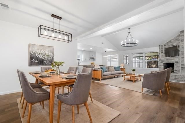 dining room featuring vaulted ceiling with beams, a fireplace, a chandelier, and hardwood / wood-style flooring