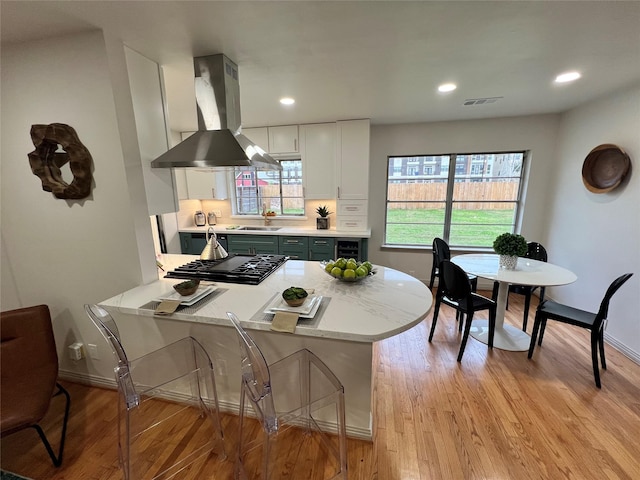 kitchen featuring island exhaust hood, kitchen peninsula, stainless steel gas cooktop, sink, and white cabinetry