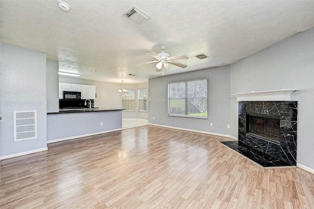 unfurnished living room featuring sink, light hardwood / wood-style flooring, ceiling fan, a fireplace, and a textured ceiling