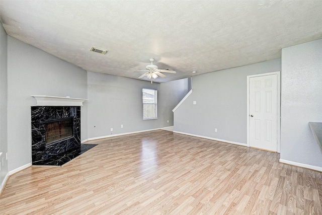 unfurnished living room featuring a premium fireplace, ceiling fan, a textured ceiling, and light wood-type flooring