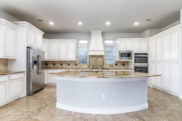 kitchen with light stone countertops, appliances with stainless steel finishes, sink, a center island with sink, and white cabinets