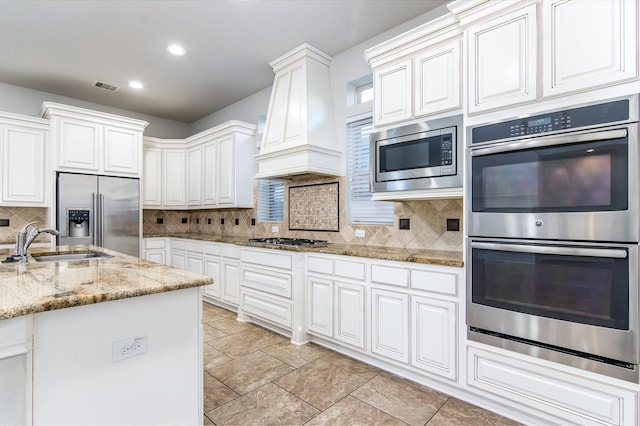 kitchen with tasteful backsplash, custom range hood, stainless steel appliances, sink, and white cabinetry