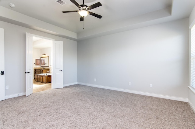 unfurnished bedroom featuring ceiling fan, a raised ceiling, light colored carpet, and ensuite bath