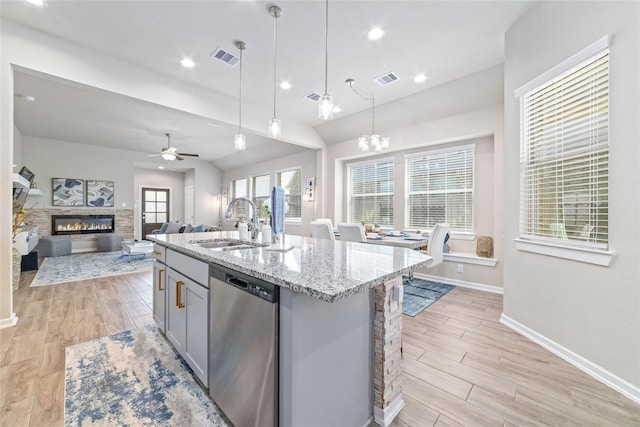 kitchen with a fireplace, a kitchen island with sink, sink, dishwasher, and hanging light fixtures