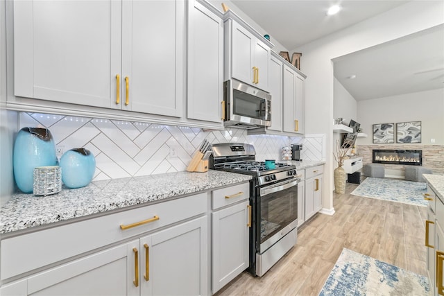 kitchen featuring light stone countertops, a fireplace, tasteful backsplash, light hardwood / wood-style floors, and stainless steel appliances