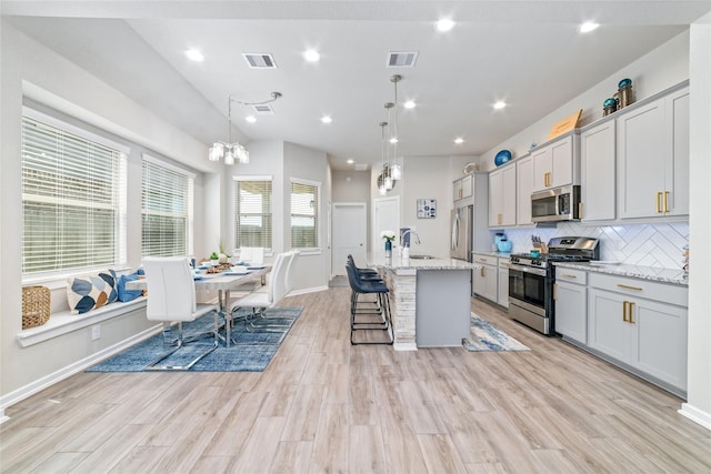 kitchen with a center island with sink, light stone countertops, appliances with stainless steel finishes, and light hardwood / wood-style flooring