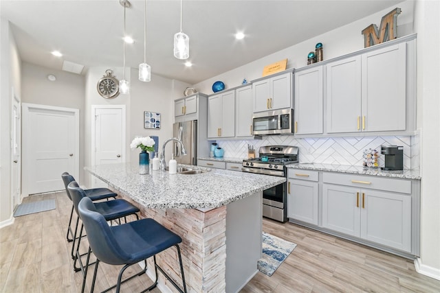 kitchen featuring hanging light fixtures, decorative backsplash, light stone countertops, an island with sink, and appliances with stainless steel finishes