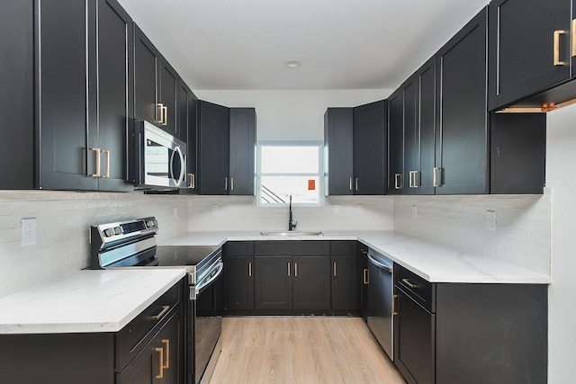 kitchen with appliances with stainless steel finishes, sink, light hardwood / wood-style flooring, backsplash, and light stone counters