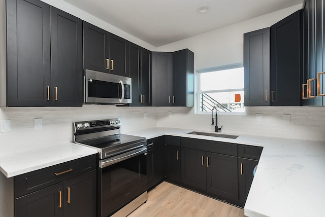 kitchen featuring stainless steel appliances, tasteful backsplash, light hardwood / wood-style floors, sink, and light stone counters