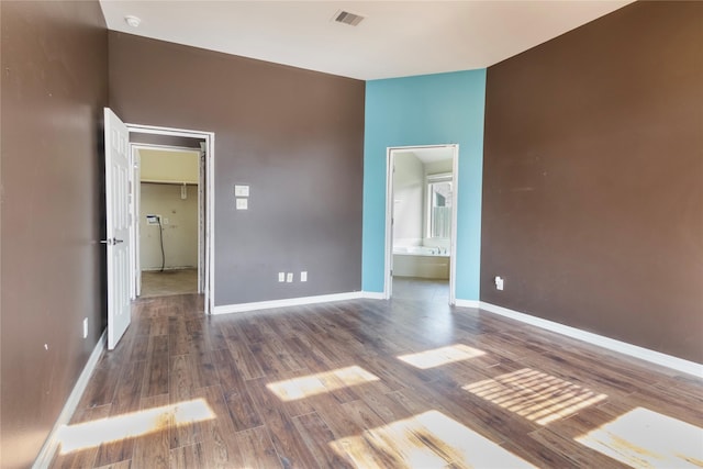 unfurnished bedroom featuring a walk in closet, ensuite bathroom, and dark hardwood / wood-style floors