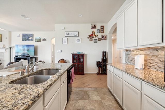 kitchen with backsplash, light stone counters, sink, black dishwasher, and white cabinetry