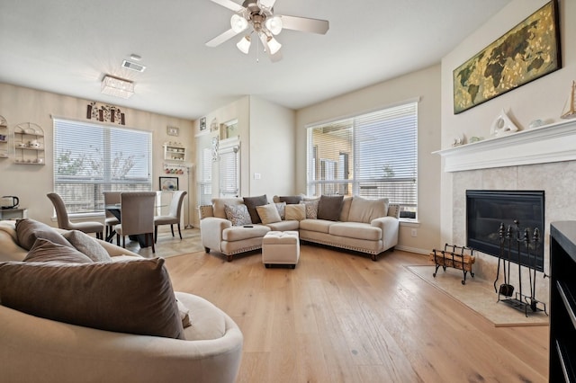 living room featuring ceiling fan, a healthy amount of sunlight, a tile fireplace, and light hardwood / wood-style flooring