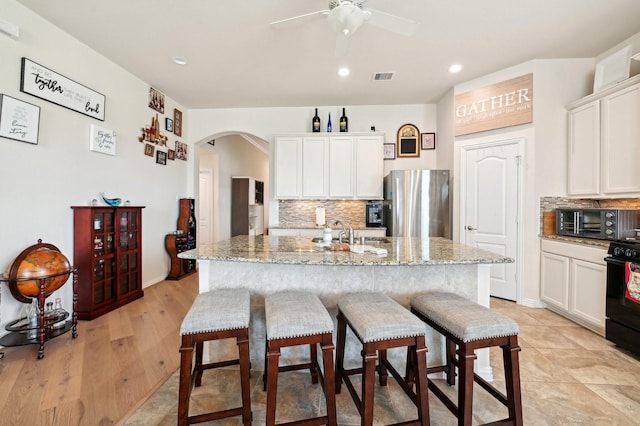 kitchen with stainless steel fridge, light stone counters, white cabinetry, and an island with sink