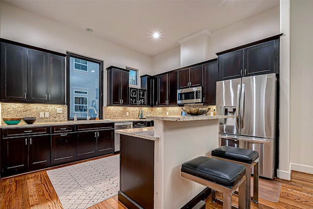 kitchen featuring light stone countertops, appliances with stainless steel finishes, a kitchen breakfast bar, light hardwood / wood-style flooring, and a center island