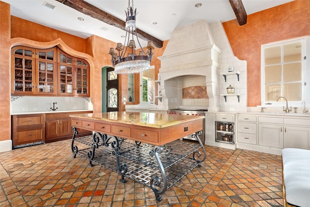 kitchen with premium range hood, sink, beam ceiling, white cabinetry, and hanging light fixtures