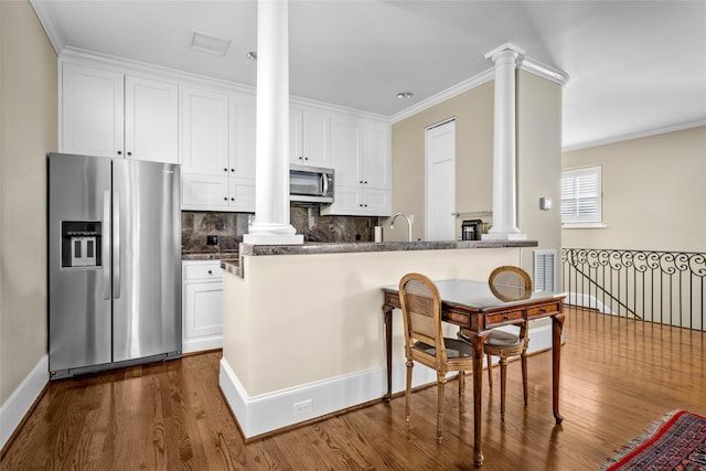 kitchen with decorative backsplash, kitchen peninsula, ornamental molding, stainless steel appliances, and white cabinets